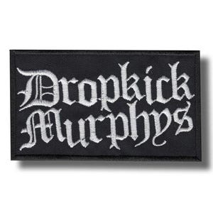 Könnte beinhalten: Schwarzer rechteckiger Aufnäher mit weiß gesticktem Text "Dropkick Murphys" in gotischer Schrift. Der Aufnäher hat einen schwarzen Rand und ist wahrscheinlich aus Stoff.