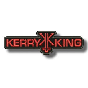 May include: Embroidered patch featuring the name "KERRY KING" in red, with a stylized symbol in the center. The text and symbol are outlined in black. The patch is rectangular with rounded corners.