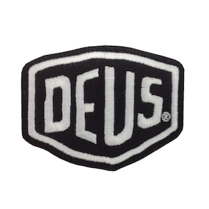 Peut inclure: Écusson brodé noir et blanc avec le mot "DEUS" en lettres stylisées et audacieuses. Le patch a une forme hexagonale distinctive avec un bord blanc. Un design simple et saisissant, idéal pour les vêtements ou les accessoires.
