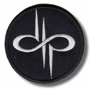 Puede incluir: Parche circular negro con un diseño bordado en blanco. El diseño presenta un símbolo de infinito entrelazado con dos líneas verticales. El parche tiene un borde negro, ideal para ropa o accesorios.