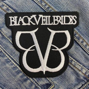 以下が含まれることがあります： 黒いパッチ。上部に白い文字で「BLACK VEIL BRIDES」と書かれ、その下に白い「BV」エンブレムが配置されています。パッチは青いデニムの背景にあります。