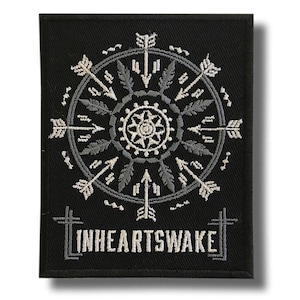 May include: Black embroidered patch with a circular design of arrows, feathers, and a central floral pattern. The text "INHEARTSWAKE" is embroidered at the bottom. The patch is rectangular and has a textured appearance.