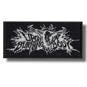 Puede incluir: Parche rectangular negro con texto bordado en blanco y un diseño de calavera. El texto dice "UPON A BURNING BODY" en una fuente gótica estilizada. El parche tiene un borde negro y es para ropa o accesorios.