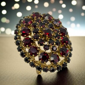 Peut inclure: Une grande broche ronde avec un sertissage en or et un groupe de pierres de grenat rouge foncé.