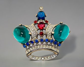 Könnte beinhalten: Eine silberne Kronenbrosche mit blauen und roten Strasssteinen und einem großen grünen Cabochonstein.