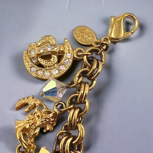 May include: Gold charm bracelet with a variety of charms, including a crystal, a crown, and a tree. The bracelet has a lobster clasp closure.