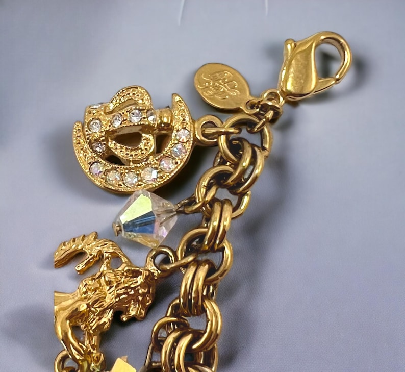 May include: Gold charm bracelet with a variety of charms, including a crystal, a crown, and a tree. The bracelet has a lobster clasp closure.
