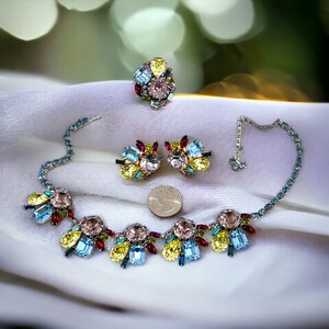 May include: A colourful multi-strand necklace featuring a cluster of blue, pink, yellow and red rhinestones. Matching earrings and a ring with a similar design are also included.