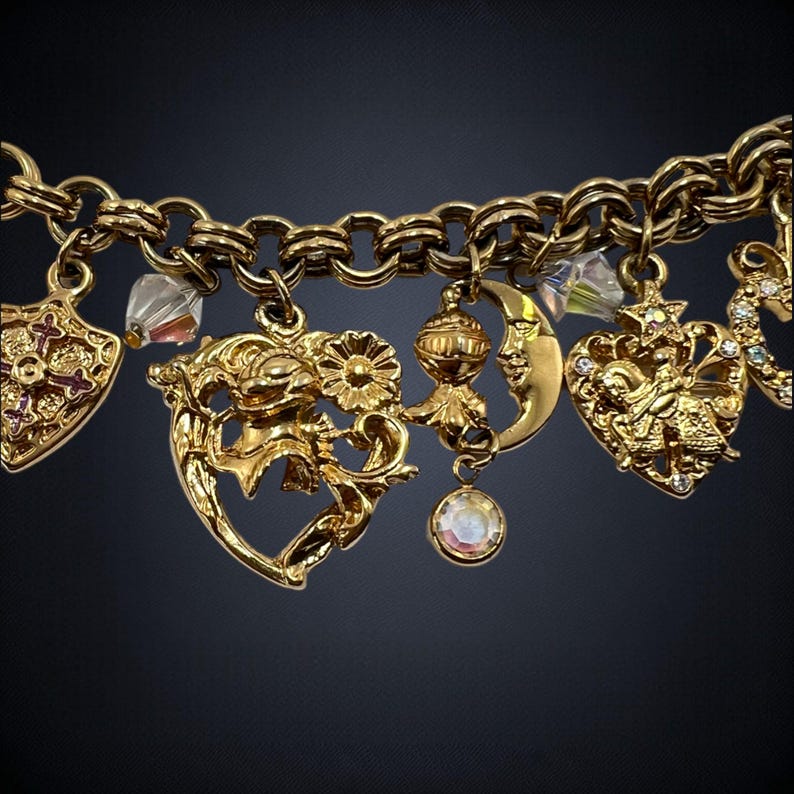 May include: A gold charm bracelet with a variety of charms, including a heart, a crescent moon, a star, and a cross. The charms are attached to a gold chain.