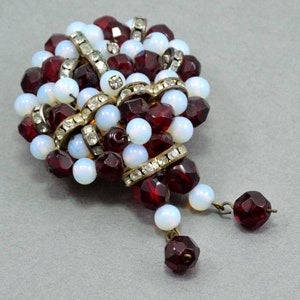 May include: A vintage brooch made of red and white glass beads with a gold tone metal setting. The brooch has a cluster of beads in the center and two dangling beads.