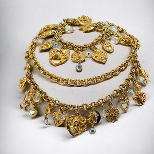 May include: A gold charm bracelet with multiple charms, including hearts, a key, and a crescent moon. The charms are attached to a gold chain with a lobster clasp.