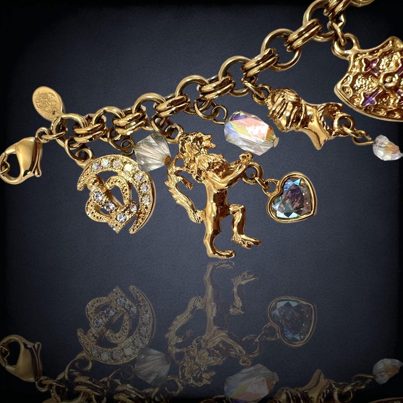 May include: A gold charm bracelet with a variety of charms, including a lion, a heart, a horseshoe, and a crown. The charms are all adorned with sparkling crystals.