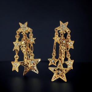 May include: A pair of gold-tone dangle earrings with multiple star-shaped charms. Each charm is adorned with clear rhinestones.