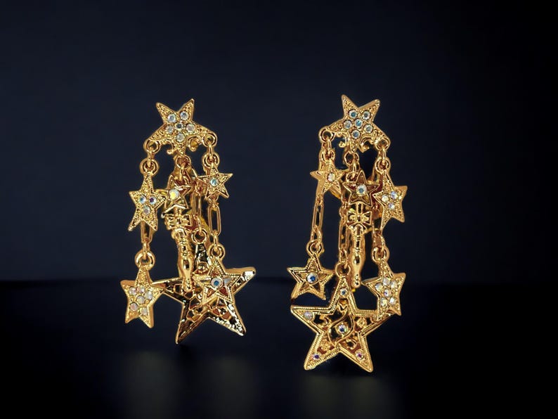 May include: A pair of gold-tone dangle earrings with multiple star-shaped charms. Each charm is adorned with clear rhinestones.