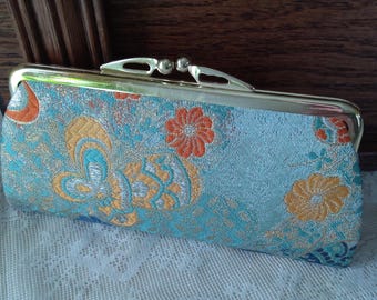 May include: A blue and gold fabric clutch purse with a floral pattern and a gold metal clasp.