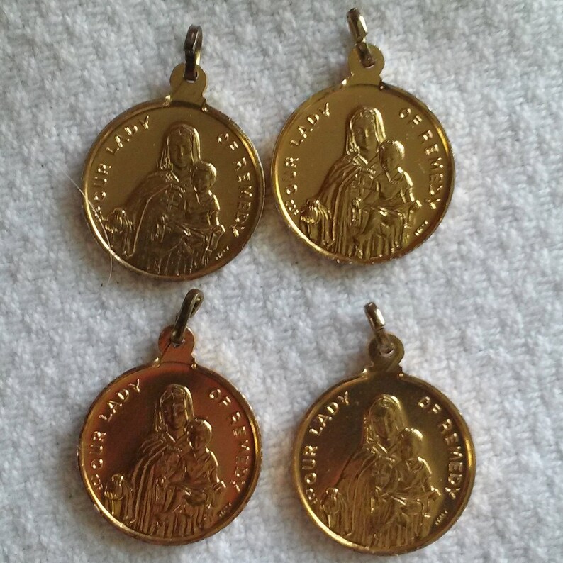 May include: Four gold-colored Our Lady of Remedy pendants. Each circular pendant features an embossed image of a woman holding a child, with the words "OUR LADY OF REMEDY" around the edge. Each pendant has a small loop at the top.