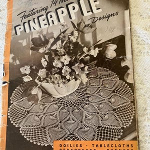 May include: Vintage book cover featuring "Pineapple Designs" with a floral arrangement on a crocheted doily. The cover includes text for doilies, tablecloths, bedspreads, and runners. The book is Book No. 230 and is priced at 10 cents.