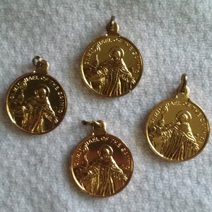 May include: Four gold-colored St. Michael of the Saints pendants. Each pendant features an image of a robed figure holding a staff, with the text "ST. MICHAEL OF THE SAINTS" around the edge. The pendants have a loop at the top for attaching to a chain.