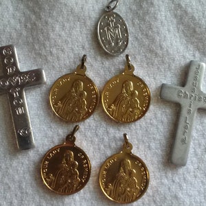 May include: Collection of religious pendants and crosses. Includes two silver crosses with engraved text, one reading "GOD LOVES YOU" and the other "JESUS IS LOVE". There are also gold-colored medallions and a silver pendant.