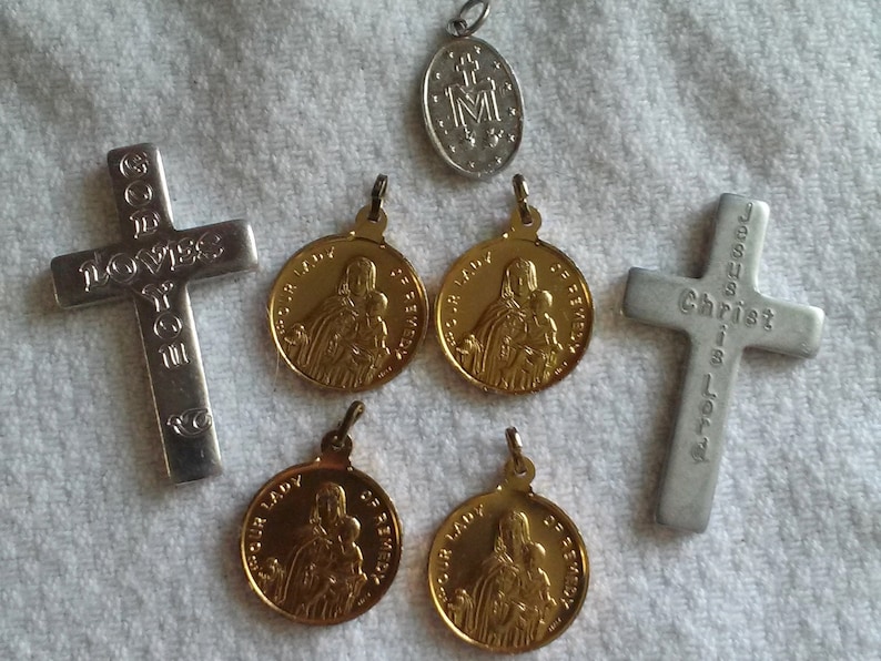 May include: Collection of religious pendants and crosses. Includes two silver crosses with engraved text, one reading "GOD LOVES YOU" and the other "JESUS IS LOVE". There are also gold-colored medallions and a silver pendant.