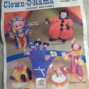 May include: A vintage crochet pattern booklet for making clown dolls and finger puppets. The cover features illustrations of various clown characters, including a jester, a pumpkin clown, and a clown with a hoop. The title of the booklet is "Clown-O-Rama Crochet and Fabric".