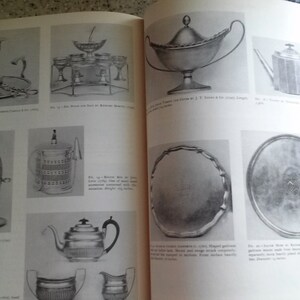May include: A book with black and white photos of antique silver serving pieces. The book includes descriptions of each piece and its maker. The book is open to a page showing a silver tea pot, a silver tray, and a silver sugar bowl.