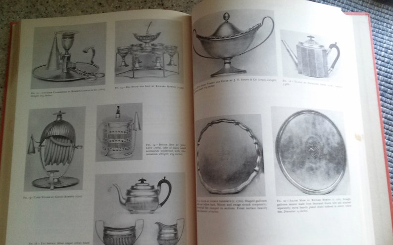 May include: A book with black and white photos of antique silver serving pieces. The book includes descriptions of each piece and its maker. The book is open to a page showing a silver tea pot, a silver tray, and a silver sugar bowl.
