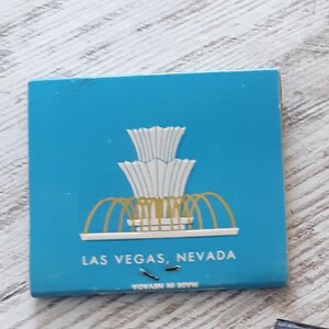 May include: A blue matchbook with a white and gold illustration of a fountain. The text "LAS VEGAS, NEVADA" is printed on the front of the matchbook.