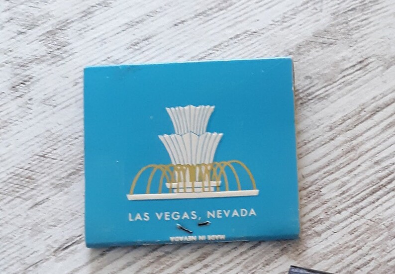 May include: A blue matchbook with a white and gold illustration of a fountain. The text "LAS VEGAS, NEVADA" is printed on the front of the matchbook.