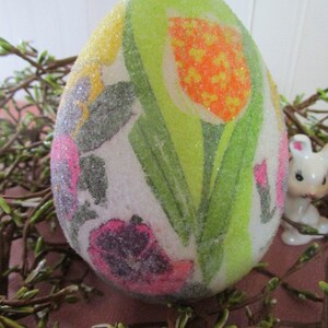 May include: A white Easter egg decorated with a sugar-coated floral design featuring tulips, leaves, and other flowers in shades of pink, green, yellow, and orange.