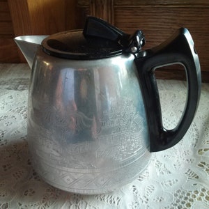 May include: A silver aluminum teapot with a black plastic handle and lid. The teapot has an embossed design of a Chinese pagoda and flowers.