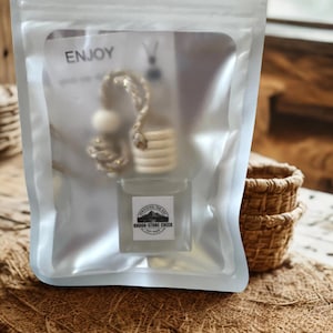 May include: An air freshener in a clear plastic package. The air freshener is a small, clear glass bottle with a wooden top and a decorative chain. The package has the word "ENJOY" printed on it, and a label that says "BROOK-STONE CREEK".