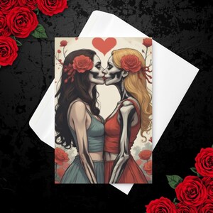Puede incluir: Una impresión artística que presenta dos figuras de esqueletos besándose, adornadas con rosas rojas en el pelo, sobre un fondo de un corazón y más rosas. La impresión está en un sobre blanco, rodeado de rosas rojas sobre una superficie negra.