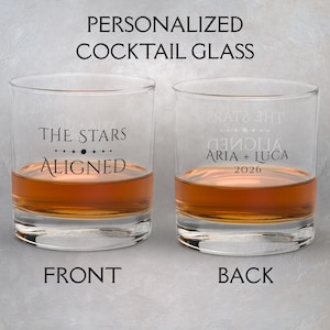 Könnte beinhalten: Zwei klare, personalisierte Cocktailgläser, gefüllt mit bernsteinfarbener Flüssigkeit. Auf dem vorderen Glas steht "THE STARS ALIGNED" und auf dem hinteren Glas "ARIA + LUCA 2026". Der Text "PERSONALIZED COCKTAIL GLASS" steht oben, mit "FRONT" und "BACK" unten.