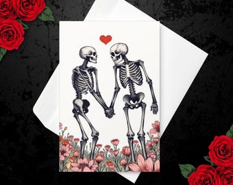 Può includere: Un biglietto d'auguri con l'illustrazione di due scheletri che si tengono per mano in un campo di fiori rosa. Un piccolo cuore rosso è posizionato sopra gli scheletri. Il biglietto è appoggiato su una busta bianca.