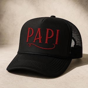 May include: Black trucker hat with the word "PAPI" embroidered in red script across the front. The hat has a curved brim, a mesh back, and an adjustable snap closure. A stylish accessory.