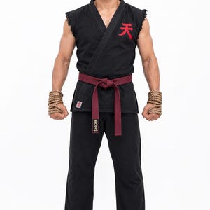 May include: A black martial arts uniform with a red belt and a red symbol on the chest. The uniform includes a sleeveless top and pants. The person is wearing rope around their wrists. The Japanese characters are visible on the uniform.