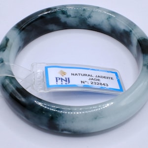 May include: A jade bangle bracelet with a marbled appearance, featuring shades of green and white. The bracelet has a smooth, polished surface. A tag with the text "NATURAL JADEITE JADE" and the number "232843" is attached.
