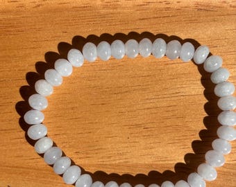 May include: A circular bracelet composed of numerous small, smooth, pale lavender-grey beads. The beads are uniform in size and shape, strung together to form a continuous loop. The surface of each bead has a subtle, semi-translucent quality.