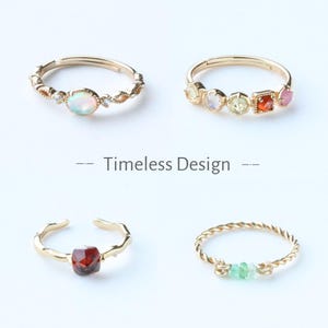 Könnte beinhalten: Vier goldfarbene Ringe mit verschiedenen Edelsteinbesätzen. Ein Ring hat einen Opal, ein anderer mehrere farbige Steine, ein dritter einen roten Edelstein und der letzte grüne Steine. Der Text "Timeless Design" wird darunter angezeigt.