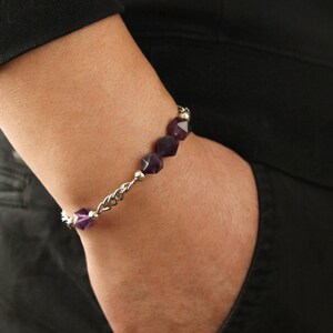 Puede incluir: Una pulsera de plata con cuentas de amatista púrpura facetadas. La pulsera presenta un delicado diseño de cadena con pequeñas cuentas de plata intercaladas entre las piedras de amatista. La pulsera se lleva en la muñeca.