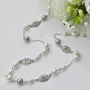 May include: Elegant pearl necklace with silver accents. The necklace features white and gray pearls, interspersed with ornate silver filigree details. The design is set against a white background with white flowers.