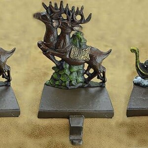 May include: Three Christmas stocking holders. Two feature brown reindeer with green foliage, and one depicts Santa Claus in a sleigh. All have a brown base with a hook for hanging stockings. The reindeer holders have gold accents.