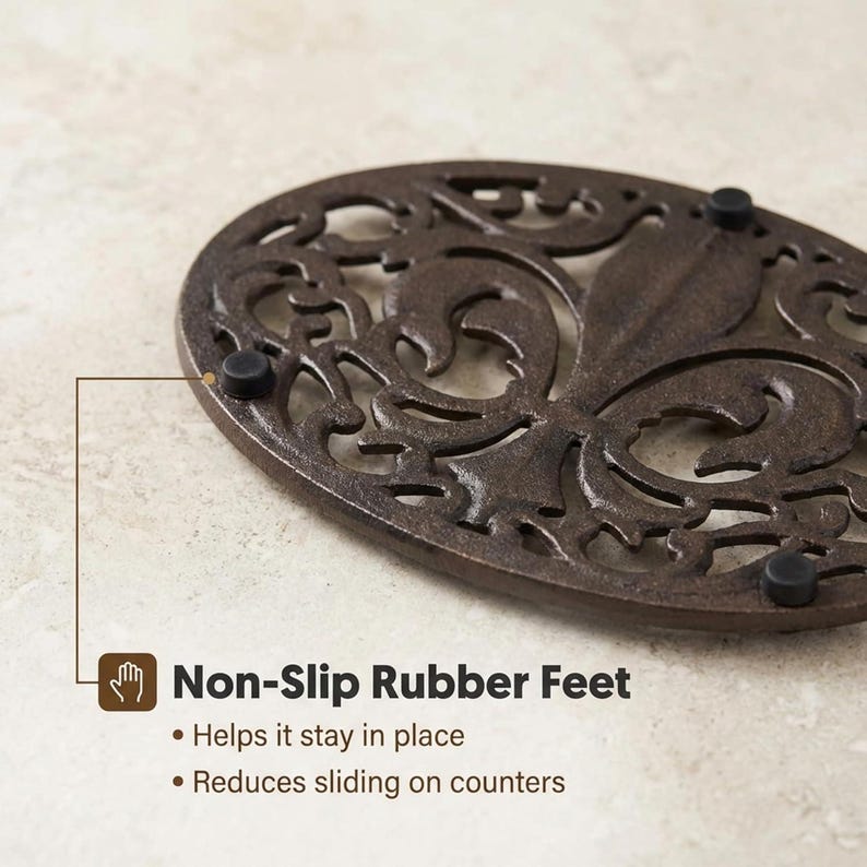 May include: Oval, cast iron trivet with an ornate, openwork design in a dark brown finish. The trivet has non-slip rubber feet to help it stay in place and reduce sliding on counters. The trivet is a kitchen accessory.