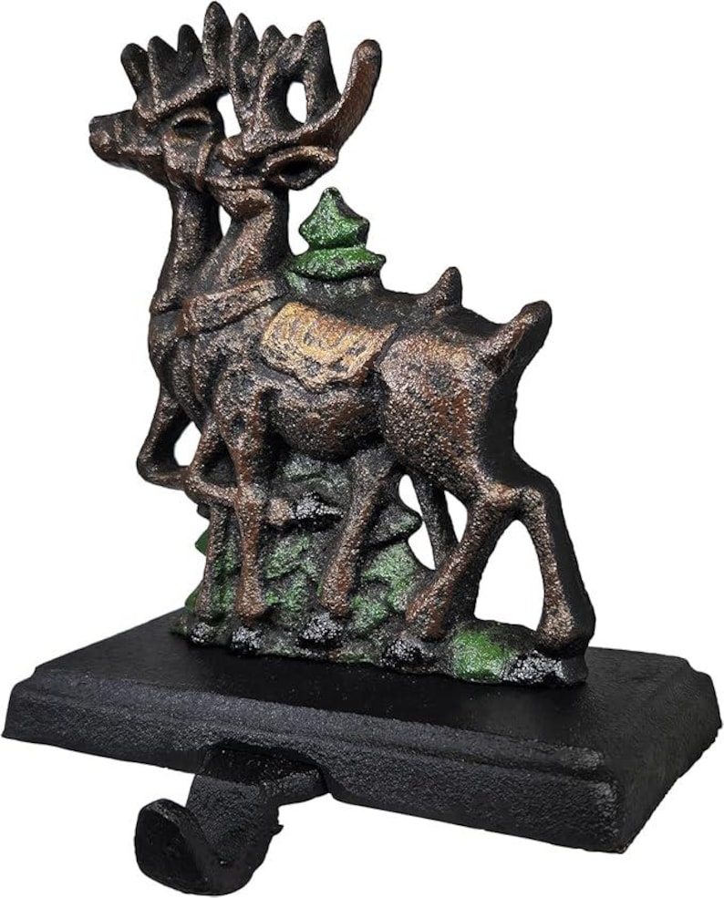 May include: A cast iron Christmas stocking holder featuring two reindeer with large antlers. The reindeer are brown with green accents and stand on a black base with a hook for hanging stockings. A small green Christmas tree is between the reindeer.