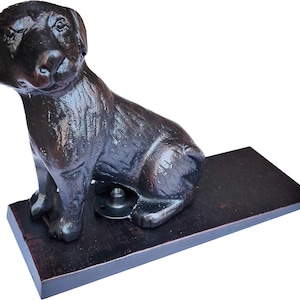 May include: A dark brown dog-shaped doorstop. The dog is sitting on a rectangular base. The doorstop is made of a dark brown material with a textured surface. The dog has a detailed face and body.