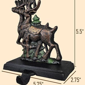 May include: A cast iron Christmas stocking holder featuring two reindeer with large antlers, a small green tree, and a black base. The holder is 5.75 inches long, 5.5 inches high, and 2.75 inches wide. The reindeer are brown with green accents.