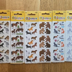 Könnte beinhalten: Sechs Stickerbögen mit Tiermotiven. Die Bögen zeigen Pferde, Bären, Katzen und Dalmatiner. Jeder Bogen ist mit "Sandy Lion Sticker Designs" in einem gelb-orangenen Design beschriftet.
