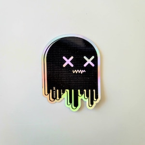 May include: A holographic sticker of a black ghost with a dripping effect. The ghost has a face with two X's for eyes and a wavy line for a mouth. The text '@trash_dot' is at the bottom of the sticker.