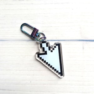 May include: A clear acrylic keychain shaped like a pixelated computer mouse cursor. The cursor is white with a thick black outline. It is attached to a small, iridescent, rainbow-colored metal lobster clasp by a matching circular jump ring.